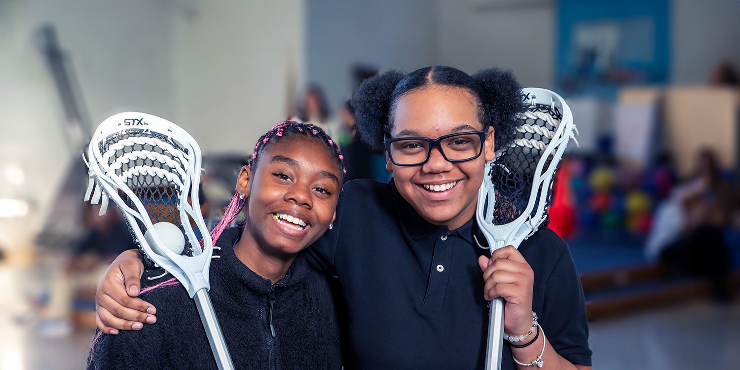 Smiling students holding a lacrosse stick
